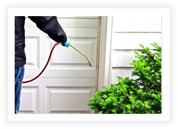 An exterminator spraying for pests on the exterior of a house, around a garage door